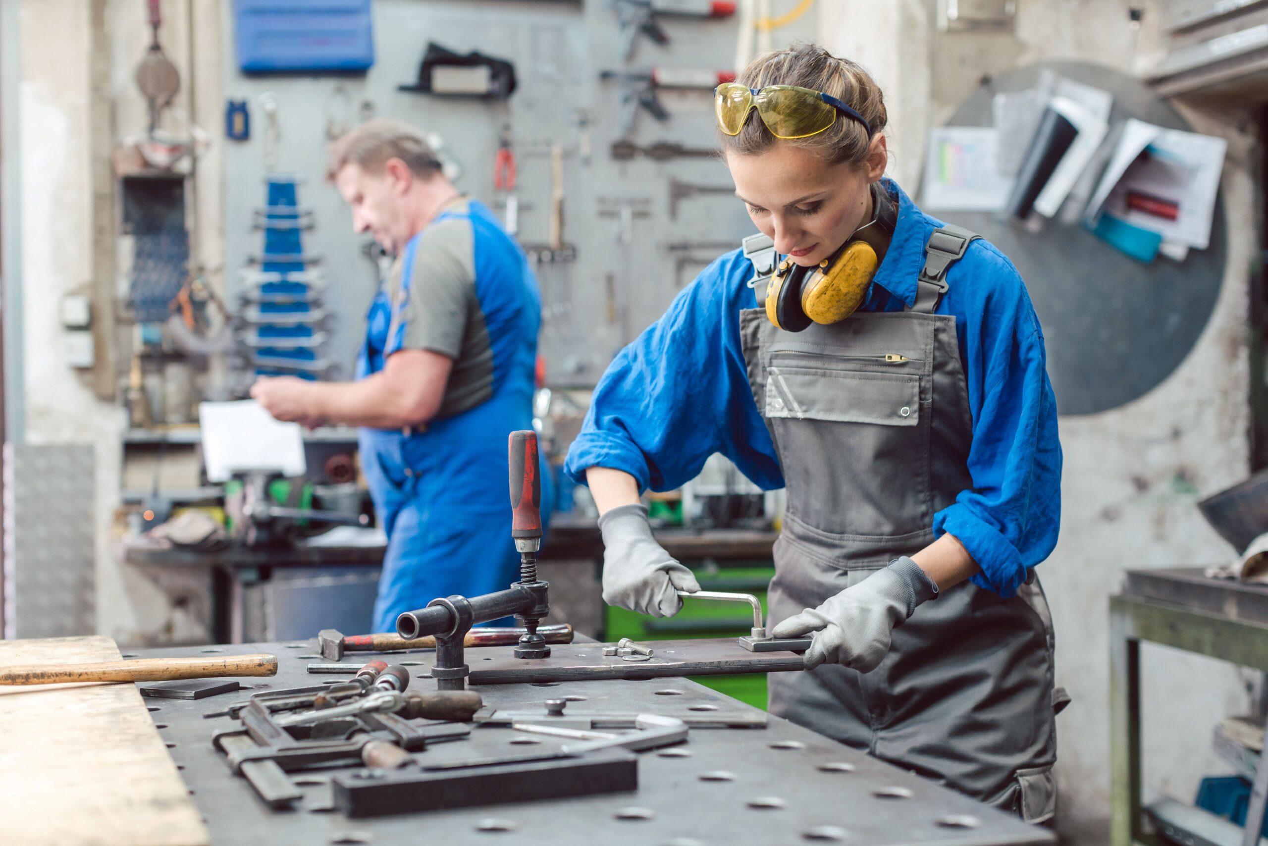 Mann und Frau arbeiten gemeinsam in einer Metallwerkstatt mit ihren Werkzeugen.